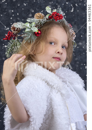 Beautiful little girl with a Christmas wreath on her head. Christmas child. 94463361