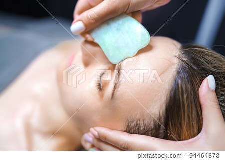 Woman having an gua sha facial massage with natural jade stone massager in the salon Woman having an gua sha facial massage with natural jade stone massager in the salon 94464878