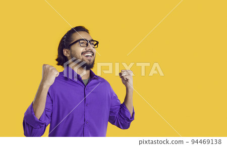 Smiling young South Asian man raises hands as sign successful, standing in yellow studio 94469138