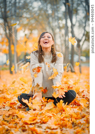 Laughing young woman having fun in autumn park playing with fallen leaves 94469845