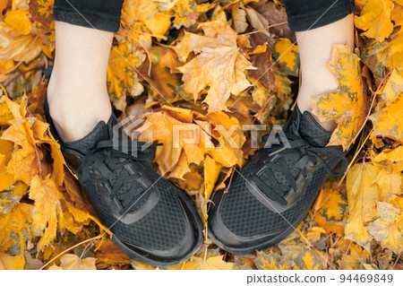 Top view of casual woman black sneakers in the autumn leaves Top view of casual woman black sneakers in the autumn leaves 94469849