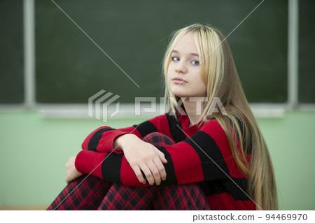 Teenager of senior school age. A teenage girl sits on the background of a blackboard and looks at the camera. Teenager of senior school age. A teenage girl sits on the background of a blackboard and looks at the camera. 94469970
