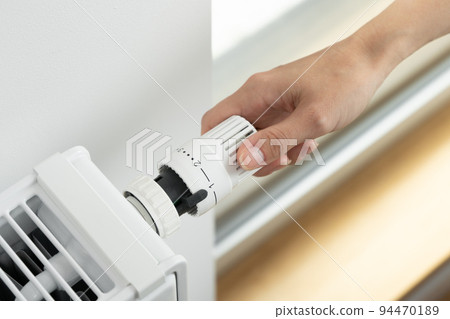 The woman lowers the radiator temperature to an economical heating mode The woman lowers the radiator temperature to an economical heating mode 94470189