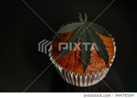 Cannabis food cake with cannabis leaf marijuana herb on dark background, delicious sweet dessert cupcakes with hemp leaf plant THC CBD herbs food snack and medical concept 94470504