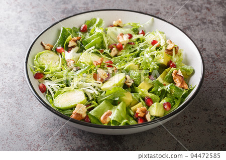 Dietary raw vegetable salad of brussels sprouts, avocado, cabbage, lettuce, pomegranate and nuts close-up in a plate. horizontal Dietary raw vegetable salad of brussels sprouts, avocado, cabbage, lettuce, pomegranate and nuts close-up in a plate. horizontal 94472585