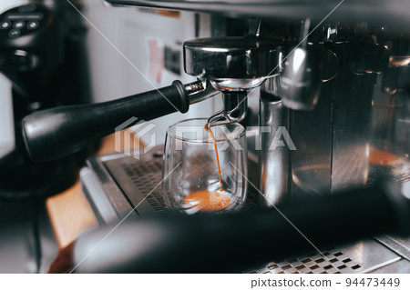 Fragrant espresso flows from a coffee machine into a cup. Making aromatic coffee with professional coffee equipment.. Fragrant espresso flows from a coffee machine into a cup. Making aromatic coffee with professional coffee equipment.. 94473449