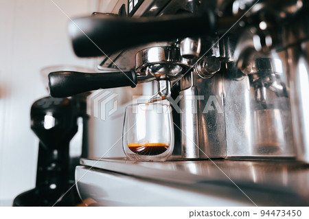 Fragrant espresso flows from a coffee machine into a cup. Making aromatic coffee with professional coffee equipment. Fragrant espresso flows from a coffee machine into a cup. Making aromatic coffee with professional coffee equipment. 94473450