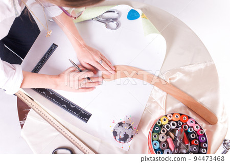 The seamstress makes a pattern for the future product. Sewing workshop. Woman engages in her favorite hobby of sewing. 94473468