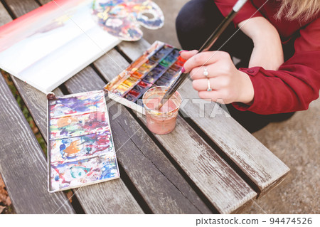 Woman draws a picture on a park bench. Blonde artist engaged in her favorite hobby of drawing. Drawing accessories.. Woman draws a picture on a park bench. Blonde artist engaged in her favorite hobby of drawing. Drawing accessories.. 94474526