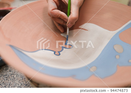 Potter woman paints a ceramic plate closeup. Girl draws with a brush on earthenware. Process of creating clay products... 94474873