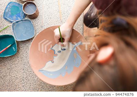 Potter woman paints a ceramic plate. Girl draws with a brush on earthenware. Process of creating clay products... 94474876