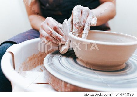 Process of creating and formation a white clay ceramic plate. Professional potter is engaged in modeling clay plates. Potter works in a workshop Process of creating and formation a white clay ceramic plate. Professional potter is engaged in modeling clay plates. Potter works in a workshop 94474889