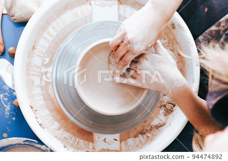 Process of creating and formation a white clay ceramic plate. Professional potter is engaged in modeling clay plates. Potter works in a workshop.. 94474892