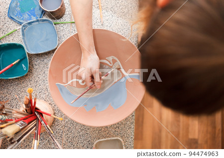 Potter woman paints a ceramic plate. Girl draws with a brush on earthenware. Process of creating clay products.. 94474963