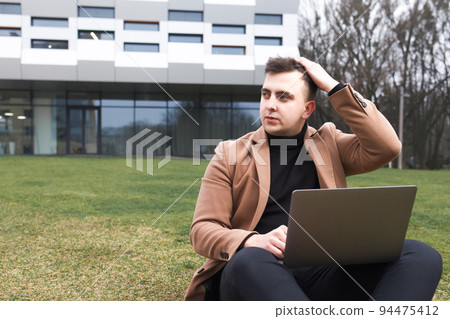 Man sitting with a laptop and depressed because of work. Pensive student holds his head.. Man sitting with a laptop and depressed because of work. Pensive student holds his head.. 94475412