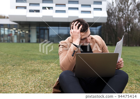 Man sitting with a laptop and depressed because of work. Pensive student holds his head. Man sitting with a laptop and depressed because of work. Pensive student holds his head. 94475414