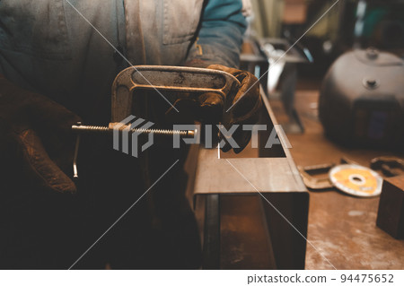 Man clamps iron products into c-clamps. Man works with clamps. Steel workshop concept. 94475652