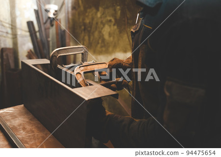 Man clamps iron products into c-clamps. Man works with clamps. Steel workshop concept. 94475654