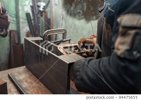 Man clamps iron products into c-clamps. Man works with clamps. Steel workshop concept. 94475655