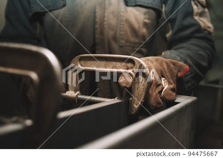 Man clamps iron products into c-clamps. Man works with clamps. Steel workshop concept. 94475667