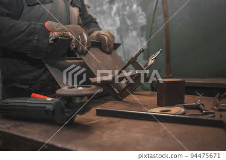 Man clamps iron products into c-clamps. Man works with clamps. Steel workshop concept. Man clamps iron products into c-clamps. Man works with clamps. Steel workshop concept. 94475671
