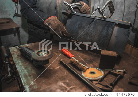 Man clamps iron products into c-clamps. Man works with clamps. Steel workshop concept Man clamps iron products into c-clamps. Man works with clamps. Steel workshop concept 94475676