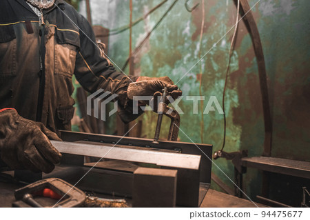 Man clamps iron products into c-clamps. Man works with clamps. Steel workshop concept. 94475677