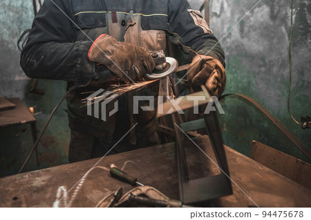 Worker does weld stripping with a grinder. Man works with iron in a workshop. Steel product manufacturing. 94475678