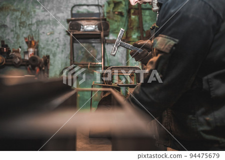 Worker with a hammer in his hands works with iron in workshop. Process manufacturing steel products. 94475679