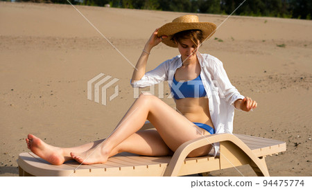 Girl on beach sunbathing sitting on sun lounger Girl on beach sunbathing sitting on sun lounger 94475774