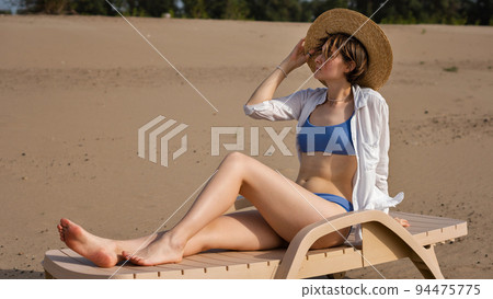 Girl on beach sunbathing sitting on sun lounger Girl on beach sunbathing sitting on sun lounger 94475775