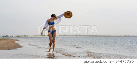 Girl in bikini walks on beach 94475780