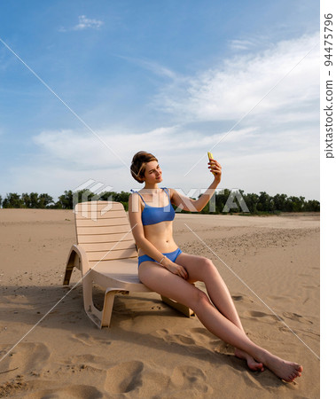 Girl on beach sunbathing sitting on sun lounger 94475796