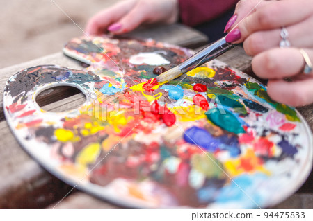 The artist who paints a picture in the park mixes paints on a palette. 94475833