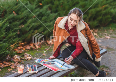Young painter draws a picture sitting in a park on the bench.. 94475844