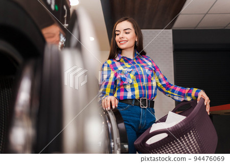 Pretty smiling woman at the laundromat holds a basket of clothes.. 94476069