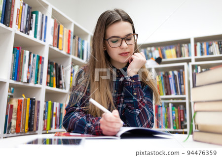 Girls writes in the library. Young student studying at the campus library.. Girls writes in the library. Young student studying at the campus library.. 94476359