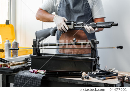 Close up of young man in apron disassembling a gun above the table Close up of young man in apron disassembling a gun above the table 94477901