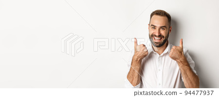 Close-up of satisfied bearded guy in white shirt, showing thumbs up in approval, like and agree, positive answer, white background Close-up of satisfied bearded guy in white shirt, showing thumbs up in approval, like and agree, positive answer, white background 94477937