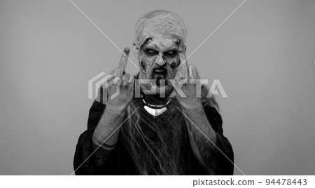 Aggressive Halloween zombie man showing around middle fingers, demonstrating protest rude gesture Aggressive Halloween zombie man showing around middle fingers, demonstrating protest rude gesture 94478443
