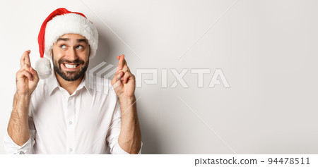 Party, winter holidays and celebration concept. Happy man in santa hat making christmas wish, cross fingers for good luck and smiling excited, white background Party, winter holidays and celebration concept. Happy man in santa hat making christmas wish, cross fingers for good luck and smiling excited, white background 94478511