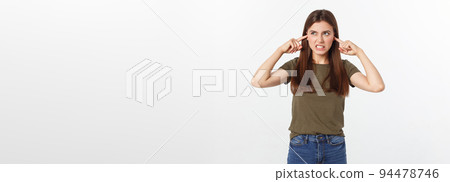 Closeup portrait of a young angry woman covering her ears, stop making that loud noise it's giving me a headache, isolated on white background. Closeup portrait of a young angry woman covering her ears, stop making that loud noise it's giving me a headache, isolated on white background. 94478746