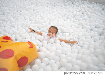 Happy little girl playing white plastic balls pool in amusement park. playground for kids. 94478776