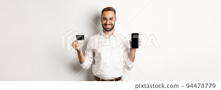 Business and online payment. Smiling handsome man showing mobile screen and credit card, standing over white background 94478779