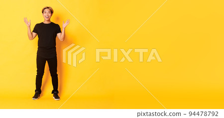 Full-length of surpirsed and excited, smiling blond asian guy raising hands up amazed, yellow background Full-length of surpirsed and excited, smiling blond asian guy raising hands up amazed, yellow background 94478792