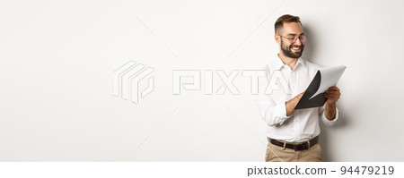 Man looking satisfied while reading documents, holding clipboard and smiling, standing over white background 94479219