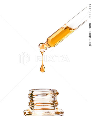 Cosmetic pipette with yellow oily drop on white bg 94479445