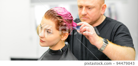 Haircut of dyed short pink wet hair of young caucasian woman by a male hairdresser in a barbershop 94479843