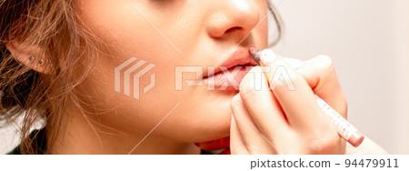 Lips makeup. Makeup artist applies contour with a pencil to the lips of a young woman in a beauty salon 94479911
