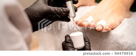 White nail polish in the hands of a manicurist while painting nails on a female feet, closeup 94479919